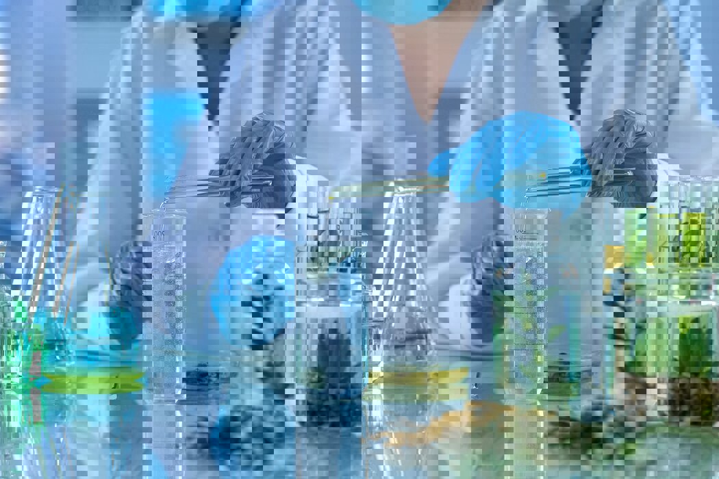 Person in a white lab coat filling a glass container from a test tube